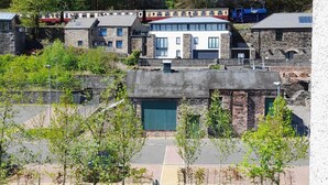 Et tog med sort røg fra skorstenen, der passerer forbi en række moderne huse med stenfacader og en grøn græsplæne i forgrunden.