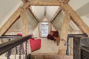 A loft bedroom with exposed wooden beams, a red chair, a wooden table, and a staircase.