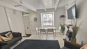 Ein modernes Wohnzimmer mit einer Couch, einem Esstisch mit Stühlen, einem an der Wand befestigten Fernseher und einer Topfpflanze.