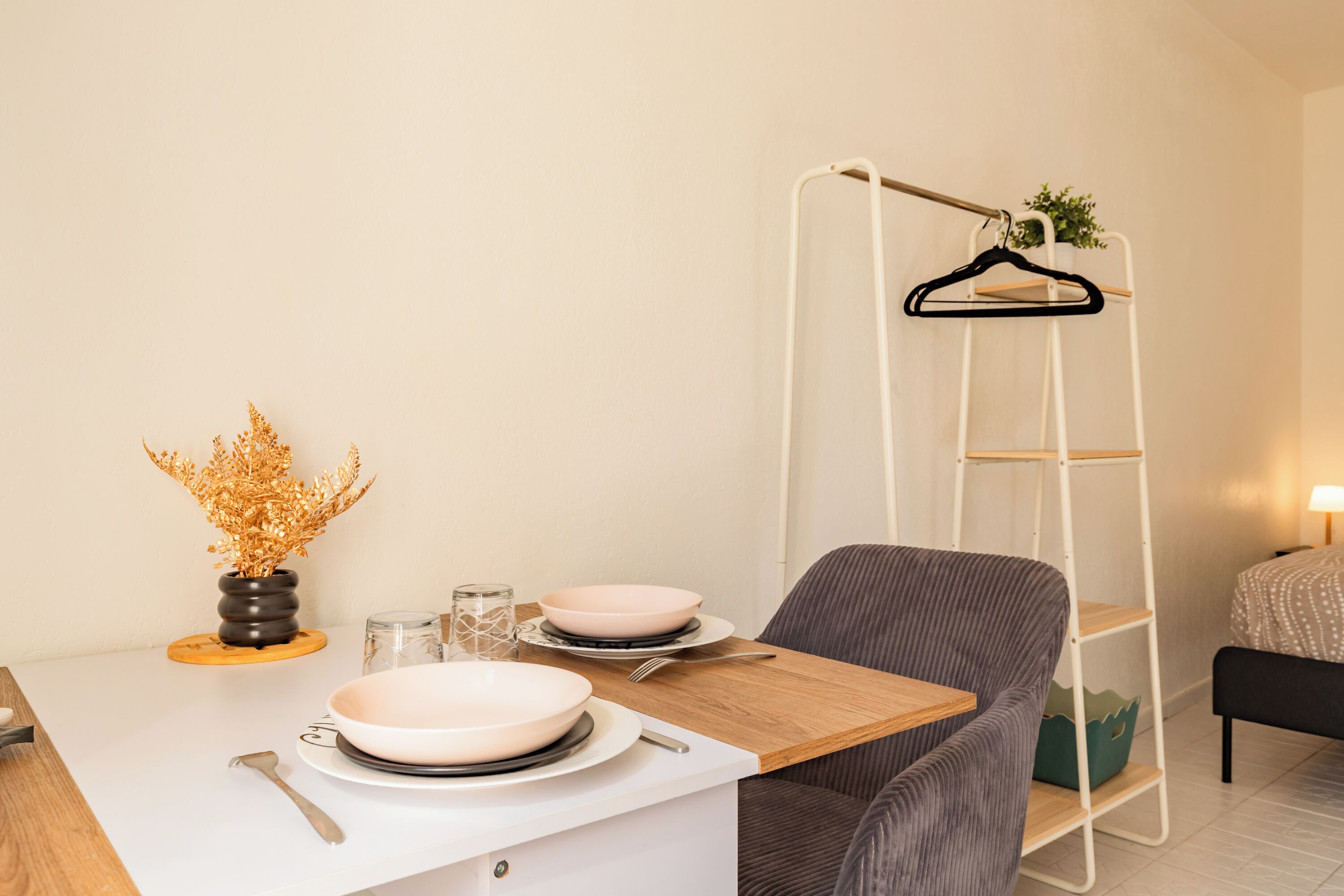 A modern dining area with a wooden table, white plates, a black hanger, and a small plant on a white shelf.