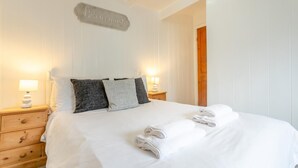 Un lit bien fait, avec du linge de lit blanc et des serviettes pliées, une table de chevet en bois avec une lampe, et une pancarte au-dessus du lit sur laquelle on peut lire : « Traitez chaque client avec le même soin. »