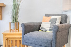 A grey armchair with a cushion, a wooden side table, and a tall plant in a vase. - 2 Bed in St. Ives (oc-b42453) (St Ives)