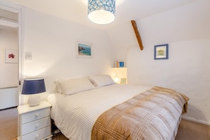 Une chambre à coucher avec un lit, une table de chevet avec une lampe, une commode et des étagères murales remplies de livres.