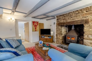 Un salon avec une cheminée en pierre, un téléviseur posé sur un meuble en bois et un canapé agrémenté de coussins à motifs.