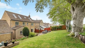 A residential property with a well-maintained lawn, a large tree, and a house with multiple windows and a sloped roof. - 4 Bed in Northleach (oc-b42441) (Northleach)