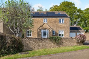Ein zweistöckiges Steinhaus mit geneigtem Dach, Solaranlagen und einer Steinmauer, die das Grundstück umgibt.