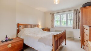 A bedroom with a wooden bed, bedside tables, a dresser, a window with curtains, and a radiator. - 4 Bed in Northleach (oc-b42441) (Northleach)