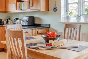 Ein Holztisch mit einer Schüssel, gefüllt mit roten Paprika, Käse und Brot, umgeben von Holzstühlen.