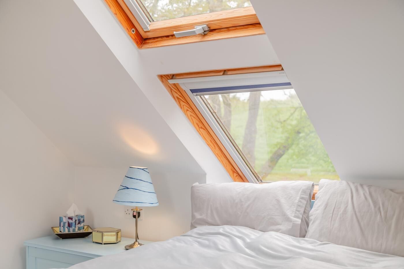 A bedroom with a skylight, a bedside table with a lamp, and a nightstand with a tissue box.