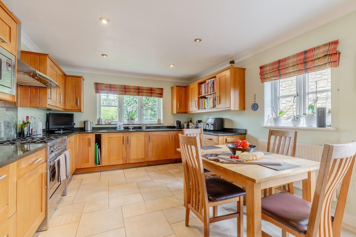 A kitchen with wooden cabinets, a dining table with chairs, and a window with a view of greenery.