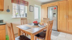 A kitchen with wooden cabinets, a dining table with chairs, a refrigerator, and a window with a view. - 4 Bed in Northleach (oc-b42441) (Northleach)