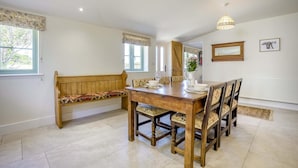 A dining area with a wooden table and chairs, a bench, and a window with curtains. - 1 Bed in Brockenhurst (oc-s40680) (Brockenhurst)