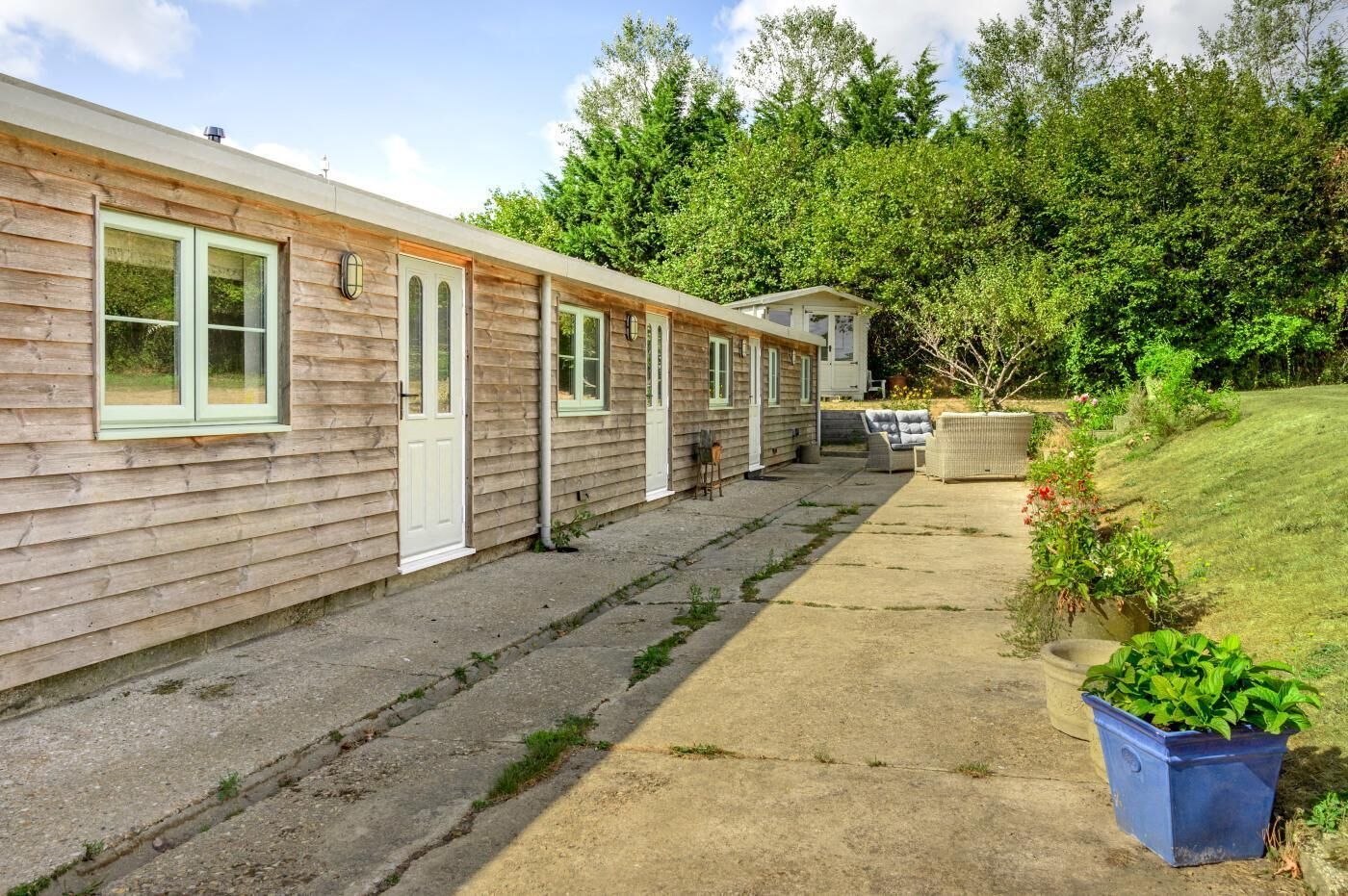 A row of wooden mobile homes with a concrete pathway leading to a grassy area with potted plants.