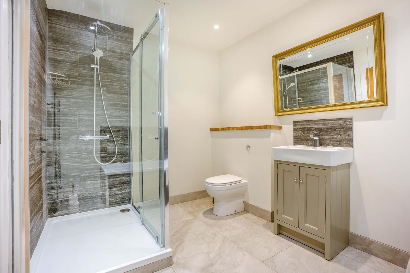 A bathroom with a glass-enclosed shower, a toilet, a sink with a wooden countertop, and a mirror with a gold frame.