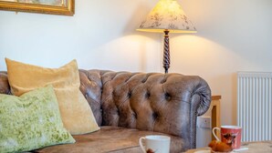 A leather sofa with cushions, a table with a cup and muffin, and a lamp. - 1 Bed in Brockenhurst (oc-s40680) (Brockenhurst)