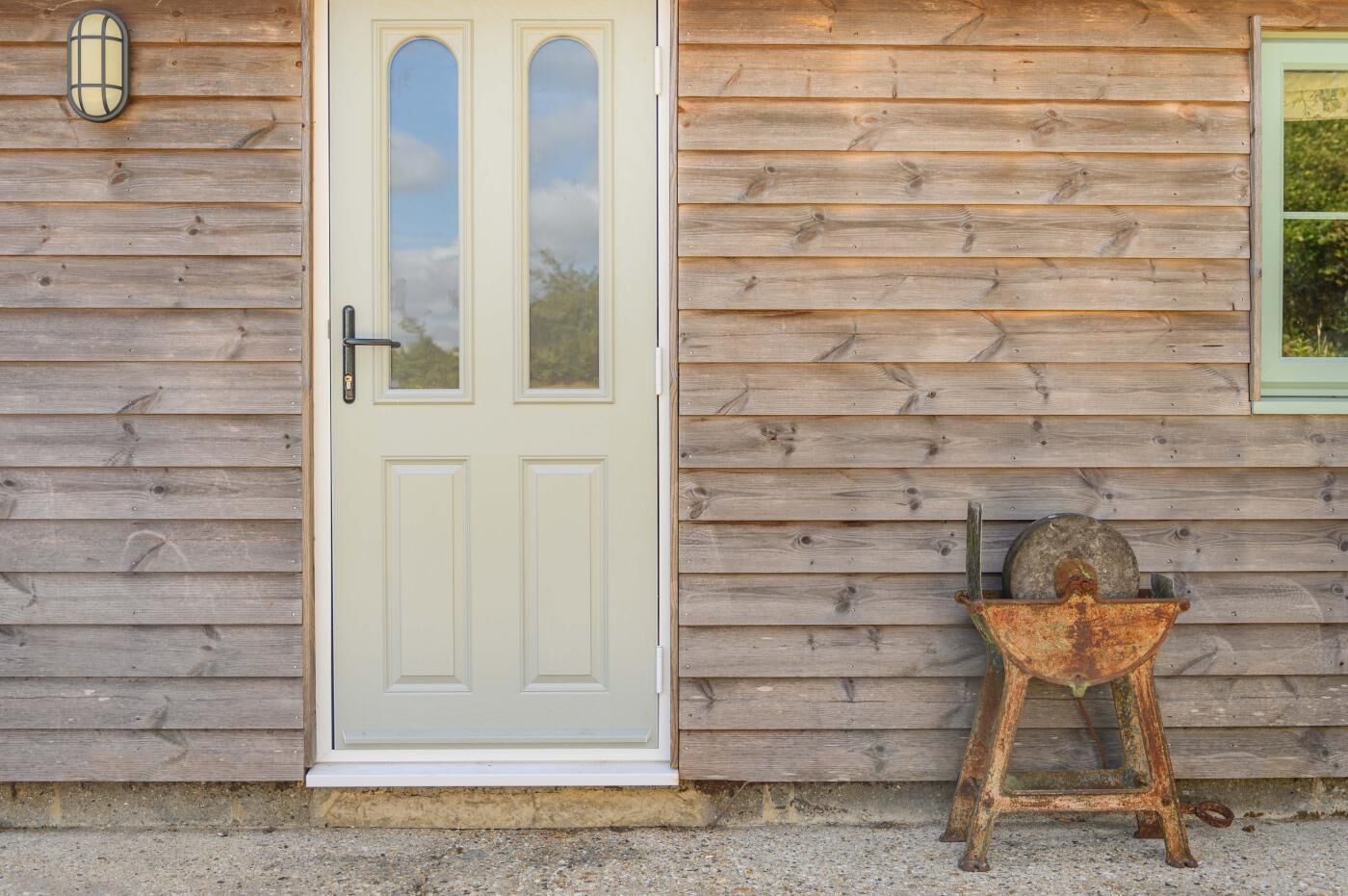 A wooden building with a white door, a small window, and a metal object on the ground.