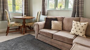 Une pièce confortable avec un canapé, deux fauteuils, une petite table ronde et une fenêtre avec des rideaux.