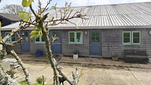 Une maison en bois à deux étages, avec un toit en métal, de nombreuses fenêtres dotées de cadres verts et un banc à l’extérieur.