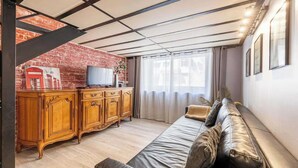 Un salon avec un mur en briques, un meuble en bois, un canapé en cuir et un téléviseur.
