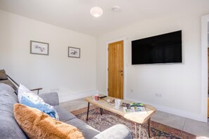 A living room with a grey sofa, a coffee table with magazines, a TV on the wall, and a wooden door. - 1 Bed in Brockenhurst (oc-f40681) (Brockenhurst)
