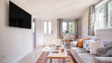 A living room with a flat-screen TV, a sofa, a coffee table, and a dining area with a table and chairs.