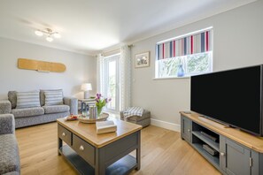 Ein Wohnzimmer mit einer Couch, einem Couchtisch, einem Fernseher und einem Fenster mit Vorhängen.
