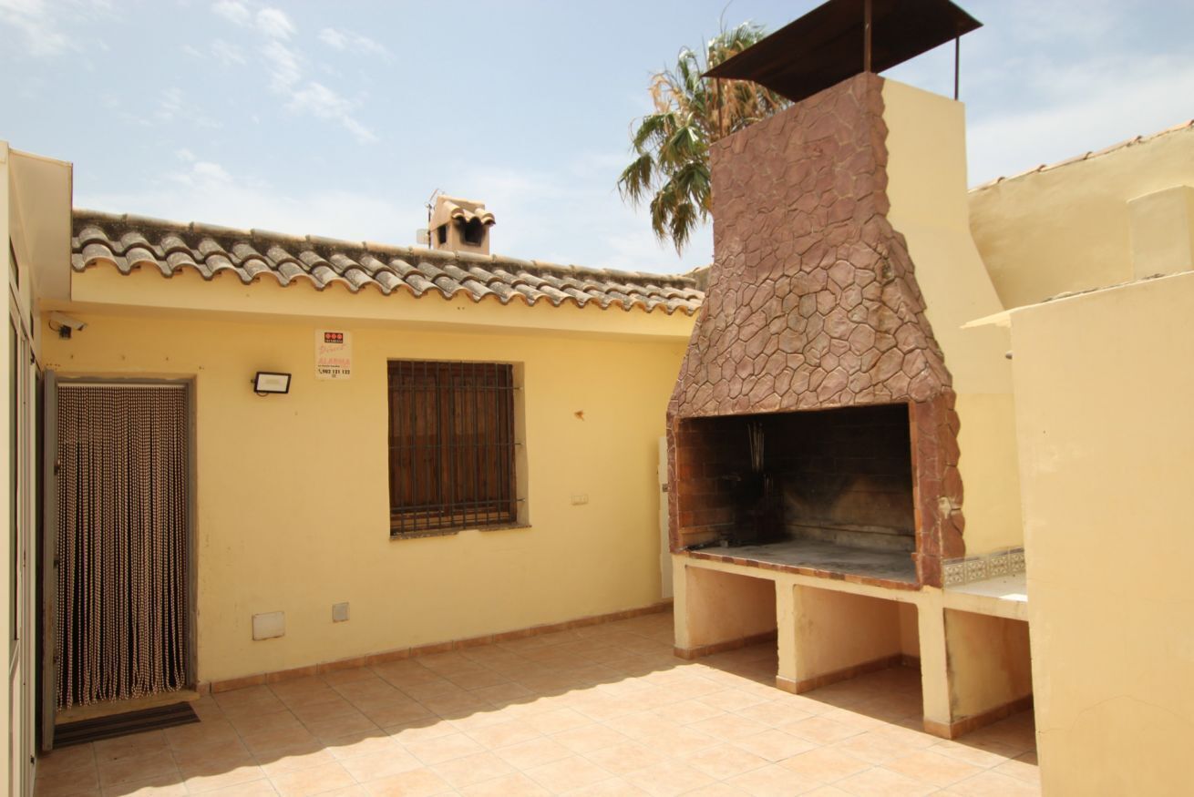 Eine Terrasse mit gemauertem Ofen, einer Tür mit Metallgitter und einem Ziegeldach.