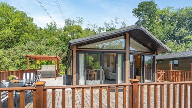 Eine moderne Holzhütte mit einer Terrasse, einem überdachten Sitzbereich im Freien und einem sichtbaren Schlafzimmer mit Bett und Fernseher.