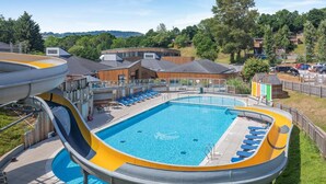Ein Swimmingpool mit Wasserrutsche, Liegestühlen und Blick auf umliegende Gebäude.