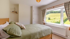 Une chambre à coucher avec un lit, un luminaire suspendu, une fenêtre avec des rideaux et une vue sur un paysage verdoyant.