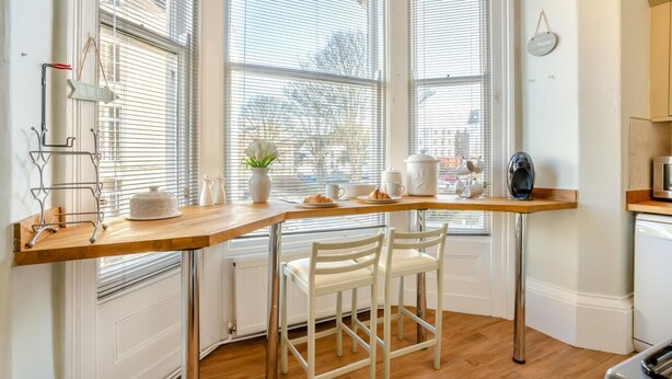 A corner kitchen with a wooden table, white chairs, a radiator, and a window with blinds. - 2 Bed in Scarborough (oc-g34248) (Scarborough)