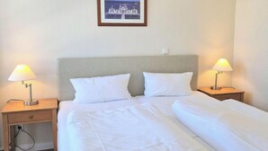 Ein Hotelzimmer mit einem Doppelbett, zwei Nachttischen mit Lampen, einem gerahmten Bild an der Wand und einer Steckdose.