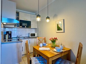 A compact kitchen with a microwave, coffee maker, and a dining area with a wooden table, chairs, and a vase of flowers. - Gemutliche Ferienwohnung Nahe Ostseestrand in Sellin (Sellin)