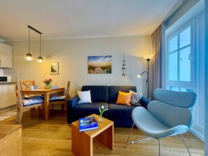 A modern living room with a sofa, armchair, dining table, and a book on a side table. - Gemutliche Ferienwohnung Nahe Ostseestrand in Sellin (Sellin)