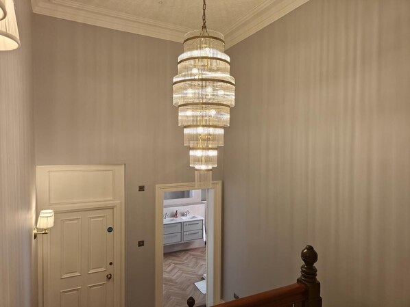 A hallway with a chandelier, a door, and a glimpse of a bathroom with a mirror and sink. - 3 Bed in Carlisle (oc-v42463) (Carlisle)