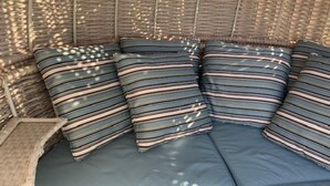 Um sofá de vime com almofadas listradas em um quarto iluminado pelo sol.