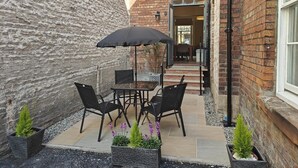 En terrasse med et bord, stole, en sort parasol og krukker med planter.