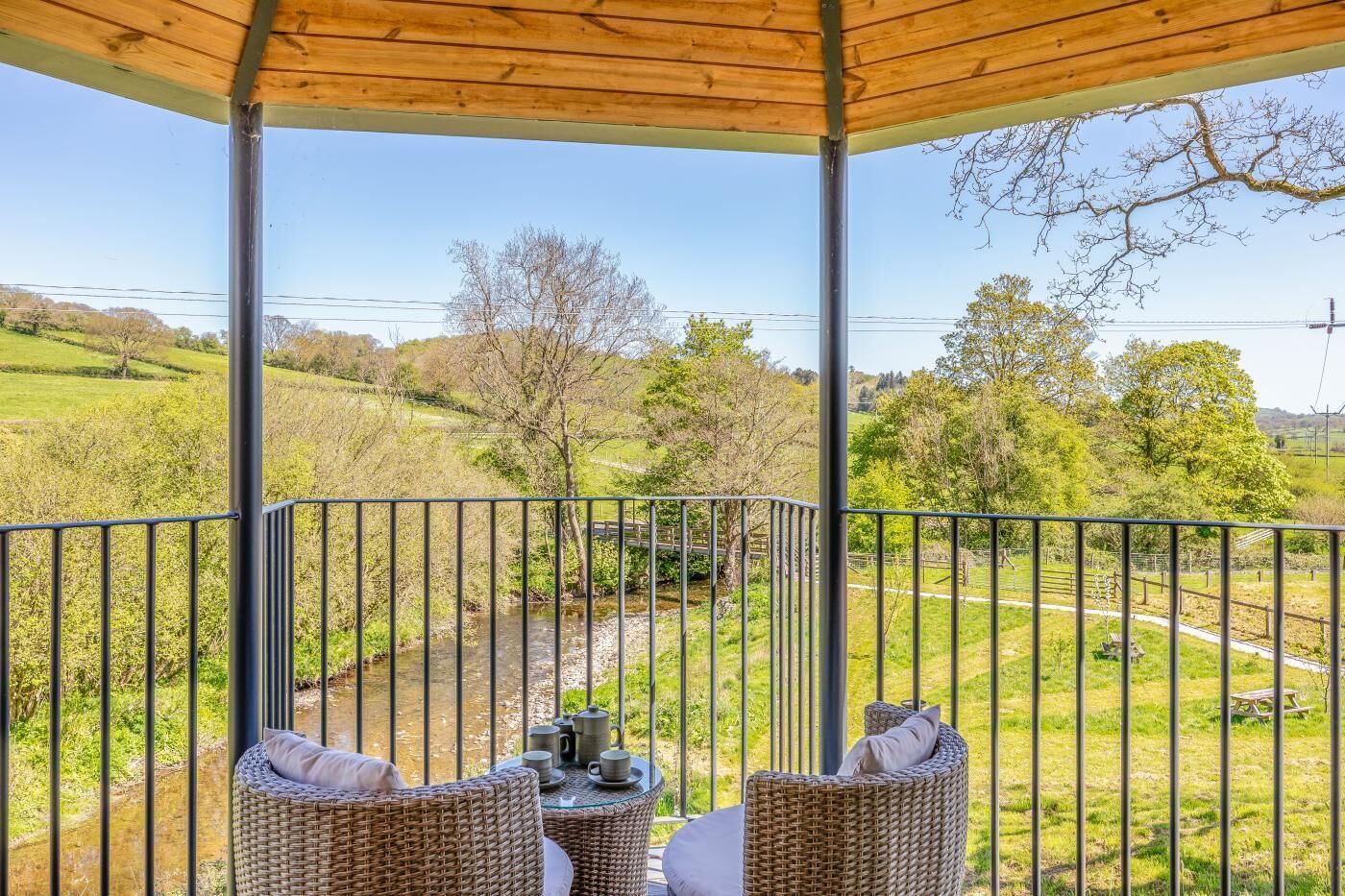 A covered outdoor seating area with wicker furniture and a view of a rural landscape.