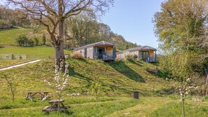 A rural setting with two wooden cabins on a hillside, surrounded by greenery and a picnic table. - 1 Bed in Aberbechan (oc-t41392) (Newtown)