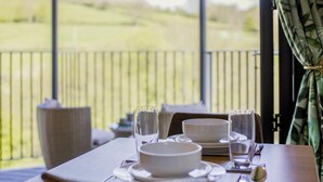 A dining table set with white plates, bowls, glasses, and cutlery on a balcony with a view of a green landscape. - 1 Bed in Aberbechan (oc-t41392) (Newtown)
