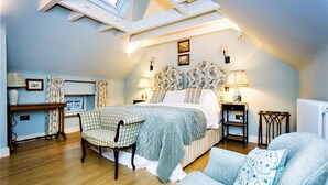 Een slaapkamer met dakraam, een bed met gestreept hoofdeinde, nachtkastjes met lampen, een stoel en een radiator.