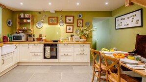 Een keuken met een centraal eiland, een eethoek met een houten tafel en stoelen, en een wand met ingelijste foto's en decoratieve borden.
