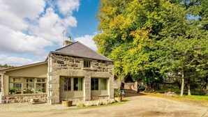 Een stenen huis met een garage, een grote boom ervoor en een heldere lucht.