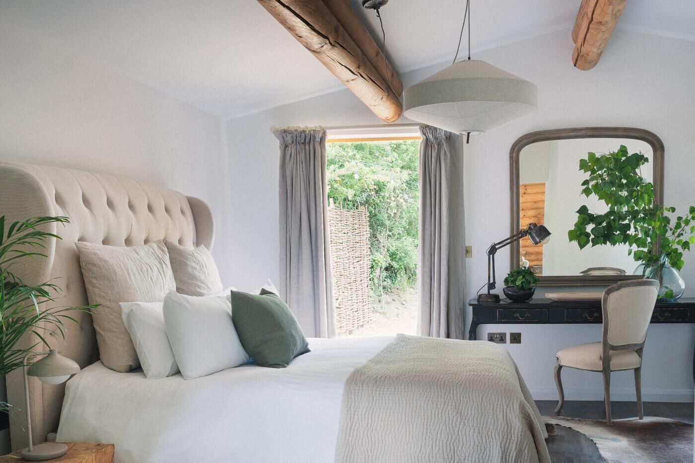 Une chambre à coucher comprenant un lit, une table de chevet, une lampe, une chaise et donnant sur un paysage verdoyant.