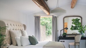 A bedroom with a bed, bedside table, lamp, chair, and a view of greenery outside.