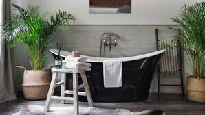 A bathroom with a freestanding bathtub, a wooden stool, a towel rack, and potted plants.