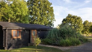 A log cabin with a wooden door and windows, surrounded by trees and grass.