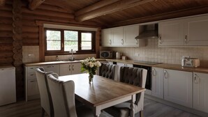 A log cabin kitchen with a dining table, chairs, a vase of flowers, and a window.