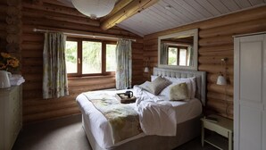 A log cabin bedroom with a bed, curtains, a bedside table, and a dresser.