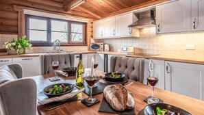 A modern kitchen with wooden ceiling beams, white cabinets, and a dining area with grey upholstered chairs.